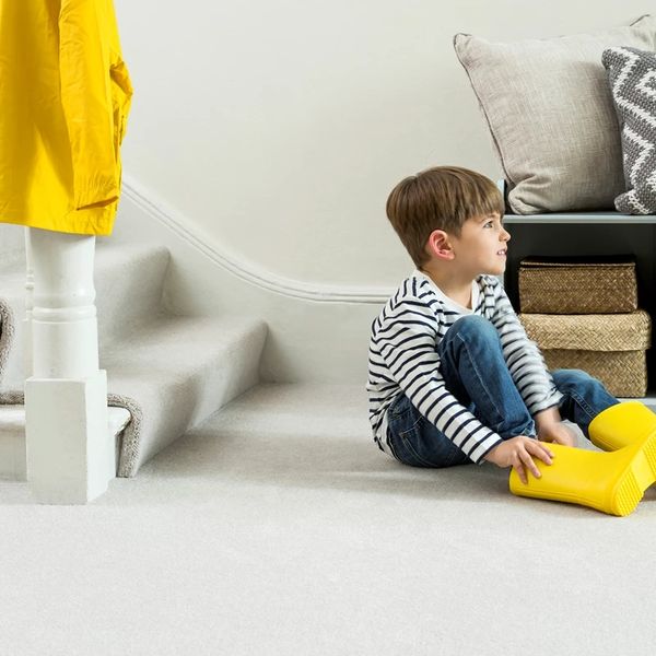 Young boy sitting on carpet putting on yellow rain boots indoors.