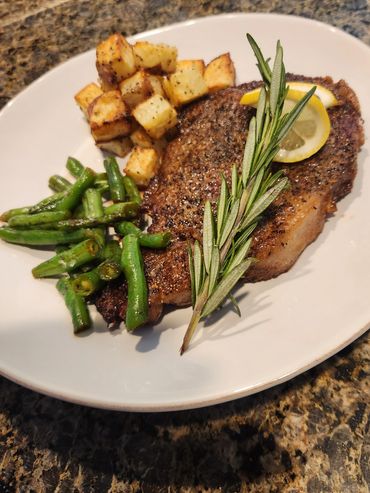 Grilled steak with lemon, rosemary, roasted potatoes, and green beans.