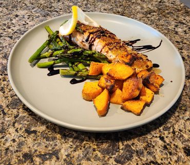 Grilled salmon with asparagus, roasted sweet potatoes, and lemon wedges on a gray plate.