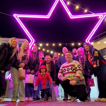 Group of friends posing under a large neon star at night.