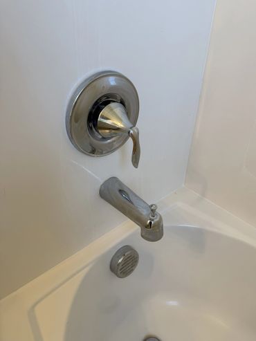 Chrome bathtub faucet and handle on a white tub wall.