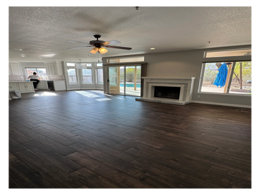 Spacious living room with dark wooden floors, fireplace, and large windows overlooking a pool.
