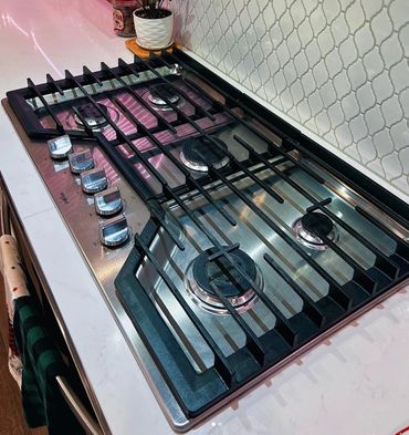 Modern stainless steel gas stove with five burners and control knobs.