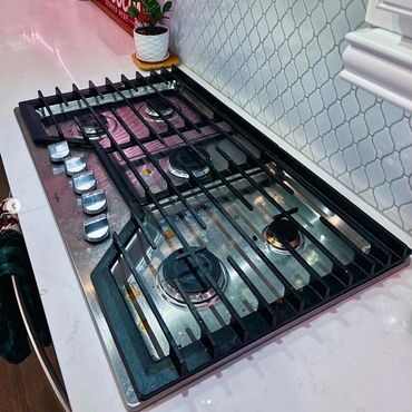 A slightly dirty stainless steel gas stovetop with five burners and control knobs on the left.
