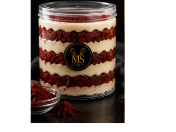 Layered red velvet cake and cream in a clear jar with a black label.