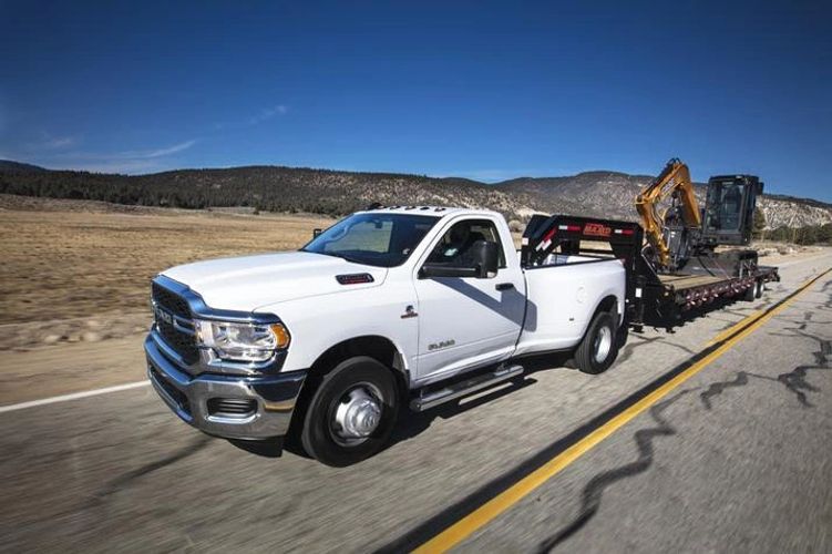 White pickup truck towing heavy construction equipment on highway.