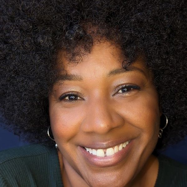 Close-up of a smiling woman with curly hair and hoop earrings.