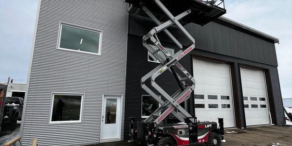 A scissor lift elevated beside a modern industrial building.