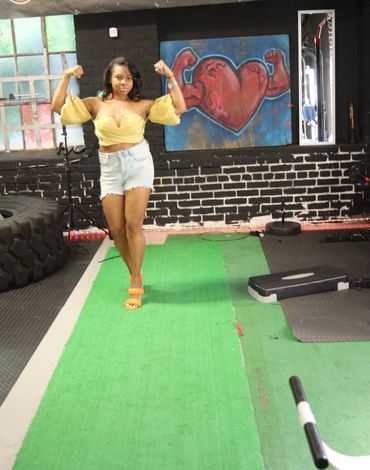 Woman flexes muscles in gym with heart and muscles artwork behind.