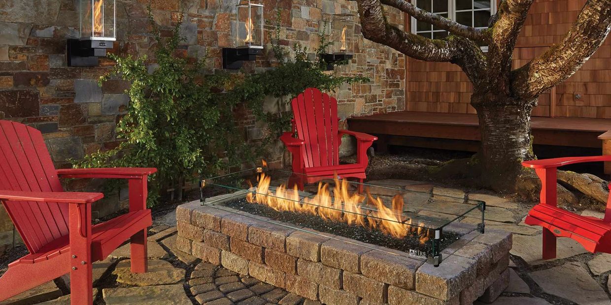 Cozy outdoor seating area with a stone fire pit and red chairs.