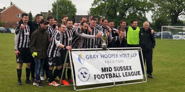 Football team celebrating with Mid Sussex Football League trophy and banner.