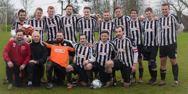 A soccer team posing together outdoors in black and white striped uniforms.