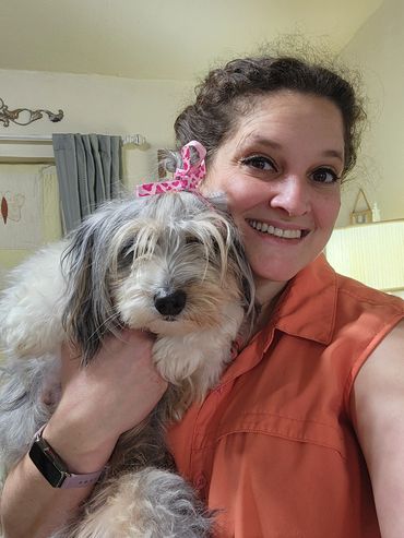 lady in pink shirt holding a fluffy dog wearing a pink bow