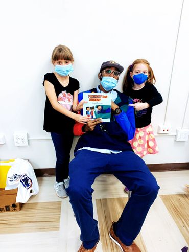 Two girls and a man wearing masks holding a book titled Present but Absent.