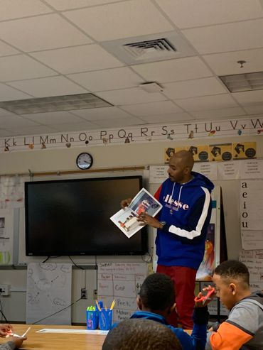 Teacher reading a book to students in a classroom setting.
