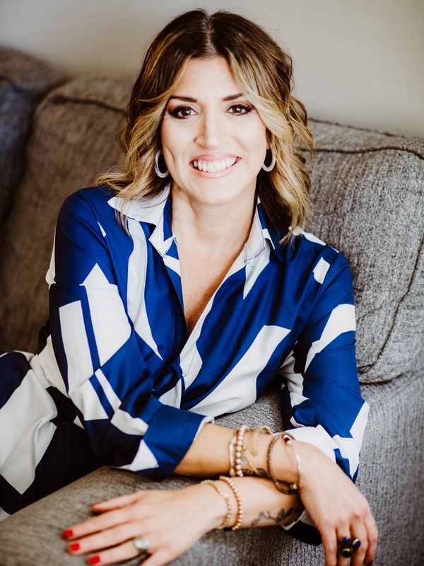 Smiling woman in a blue and white patterned blouse lounging on a gray couch.