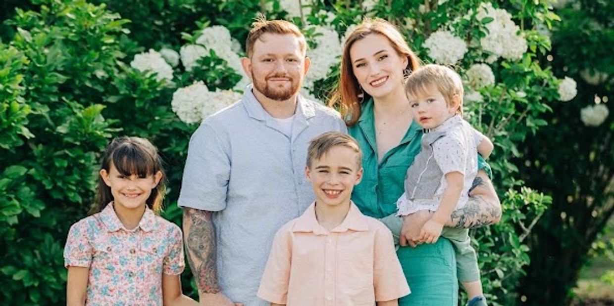 Happy family posing together outdoors with greenery and white flowers.