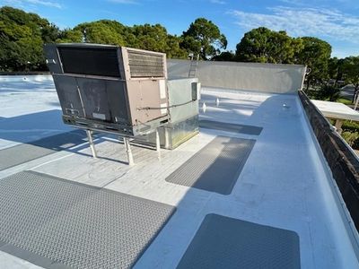 An HVAC unit on a flat commercial roof with anti-slip walk pads leading to it on a sunny day.