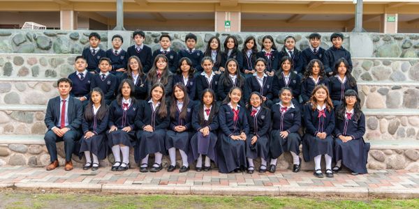 School group photo with students and a teacher seated outdoors on stone steps.
