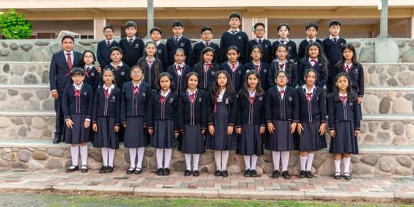 Group photo of schoolchildren in uniform with a teacher outdoors.