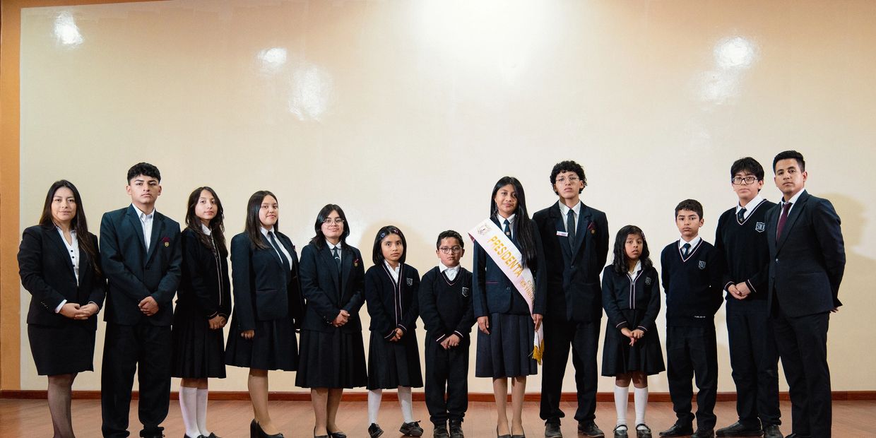Group of students and teachers in formal uniforms posing for a photo indoors.