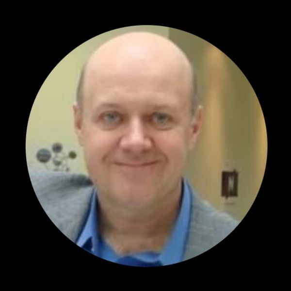 Portrait of a smiling bald man in a blue shirt and gray jacket.