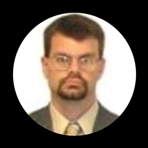 Portrait of a man with glasses and a goatee in formal attire.