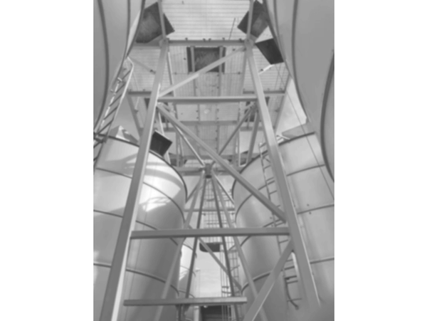 Industrial metal silos with supporting steel framework and ladders under a blue sky.