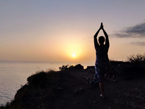 Pessoa praticando yoga ao pôr do sol à beira-mar.