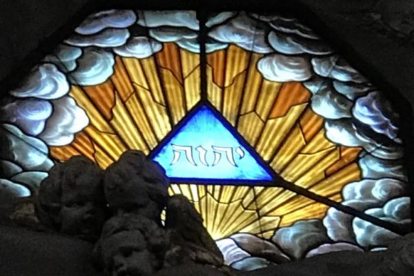 Stained glass window with a glowing triangle and Hebrew letters, also known as the tetragrammaton.
