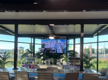 Modern indoor bar area with sleek stools and a mounted TV under a covered patio.
