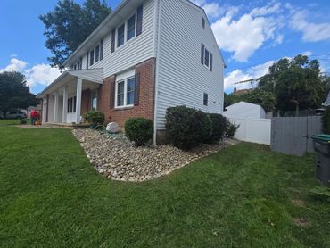 A suburban house with a stone-bordered garden and green lawn under a blue sky.