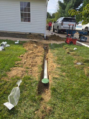 Trench with installed pipe beside a house under construction.