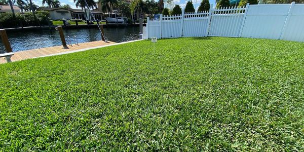 A lush green lawn next to a canal with a white fence.