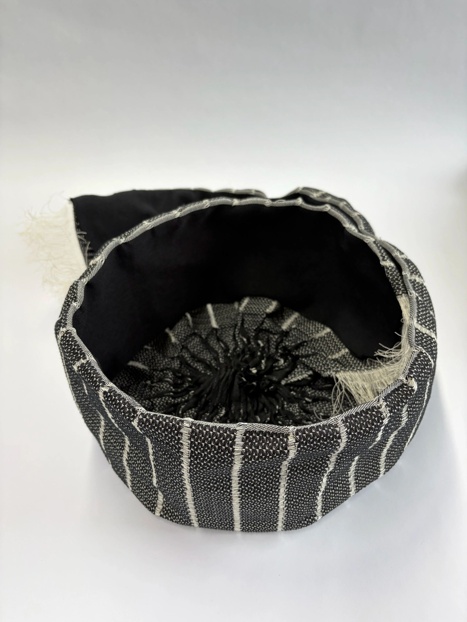 Top view of a black and white woven fabric basket with frayed edges.