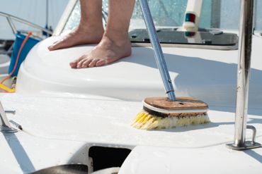 Barefoot person cleaning the deck of a white boat with a brush