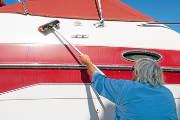 Person with gray hair cleaning the side of a boat with a long-handled brush