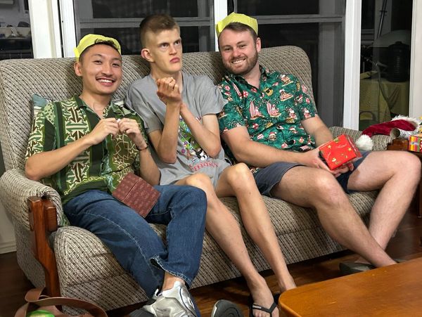 Three friends sitting on a couch, two wearing green shirts and yellow paper crowns.