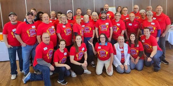 Club members in red Dining Around Greer shirts smiling for a group photo.