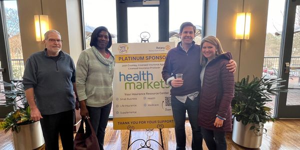 Business people standing beside their sponsor sign at event.