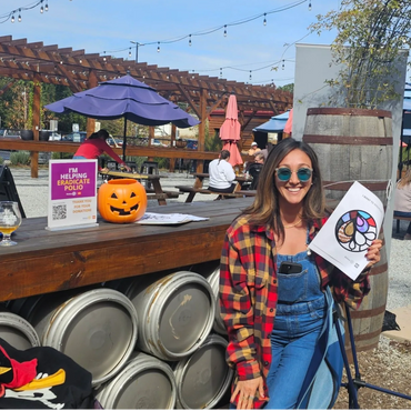 Woman smiling and holding a coloring sheet. Pumpkin bucket and sign about polio beside her