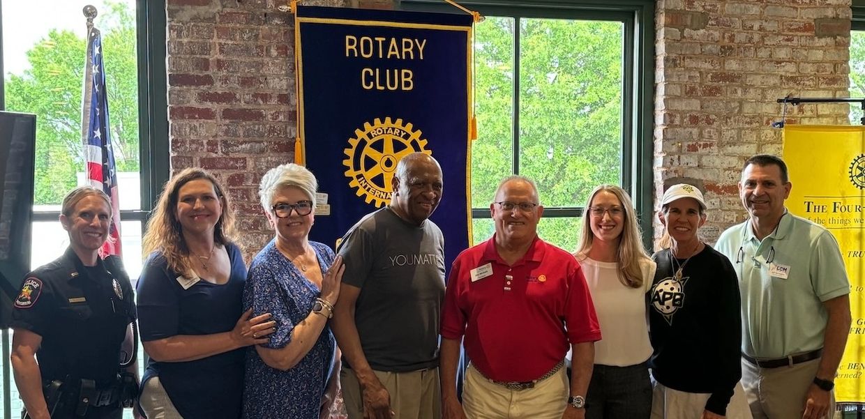8 smiling people in front of Rotary banner.