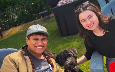 young man in baseball cap sitting beside black dog with a young woman on other side of dog