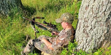 A youth hunter against a tree using a Hip Stick Shooting Rest off his knee to steady a crossbow 