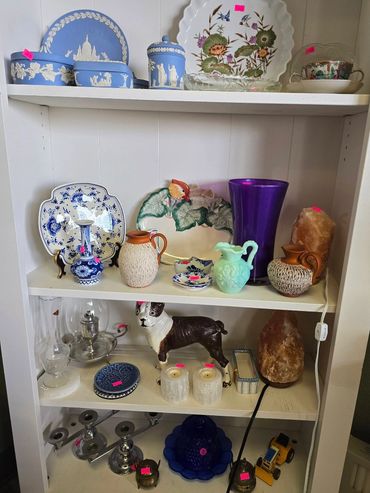 A shelf filled with assorted vintage ceramics, glassware, and decorative items.