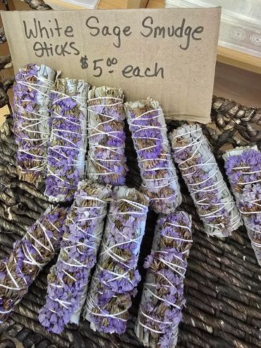 White sage smudge sticks with purple flowers in a basket, priced at $5 each.