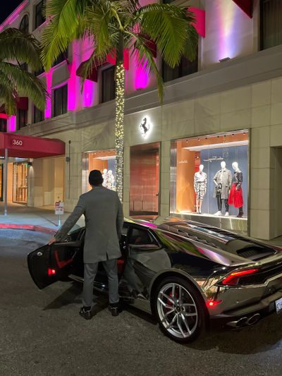 A man in a gray suit standing beside a Lamborghini Huracan