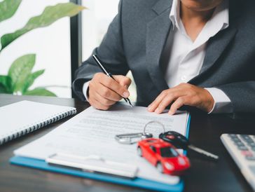 Person signing car insurance documents with model car.