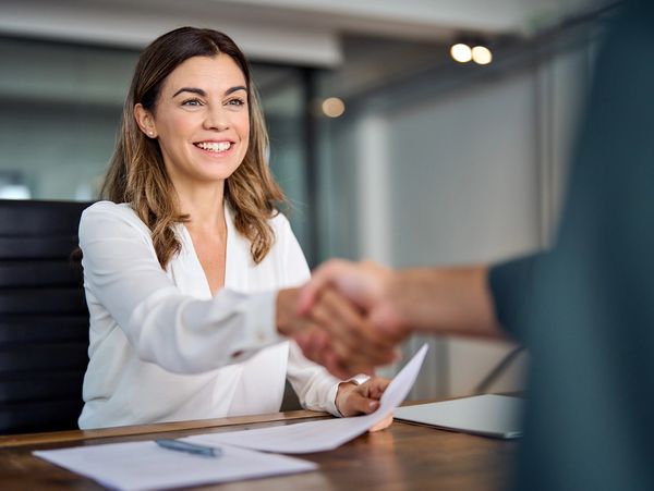 Smiling businesswoman shaking hands across a desk.