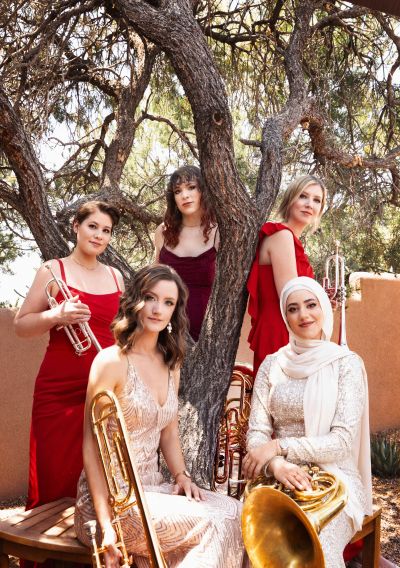 Members of Seraph Brass (quintet) sit outside under a tree with their instruments in hand